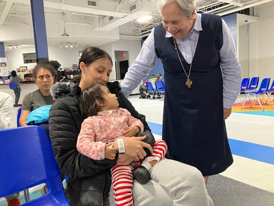 Sister Norma saluda a una persona adulta con un bebé en brazos.