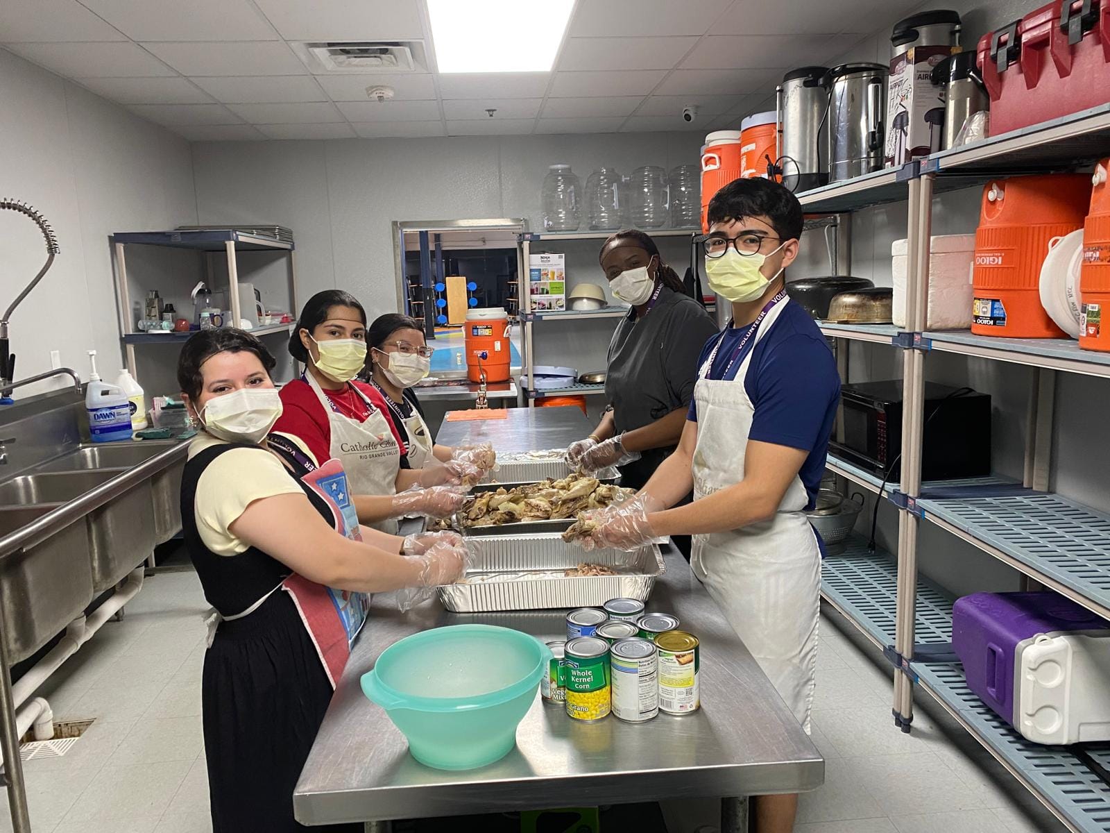 Personas con delantales preparando alimentos en una cocina.