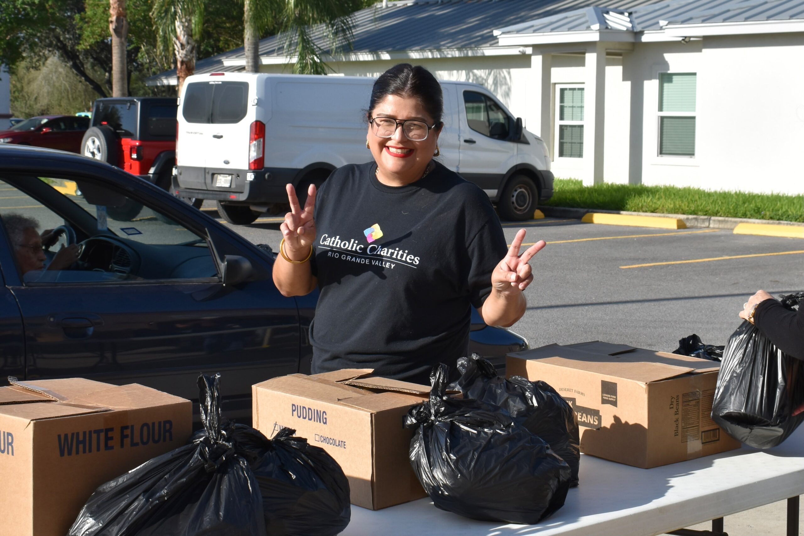 A smiling CCRGV volunteer behind food-distribution tables in Edcouch.